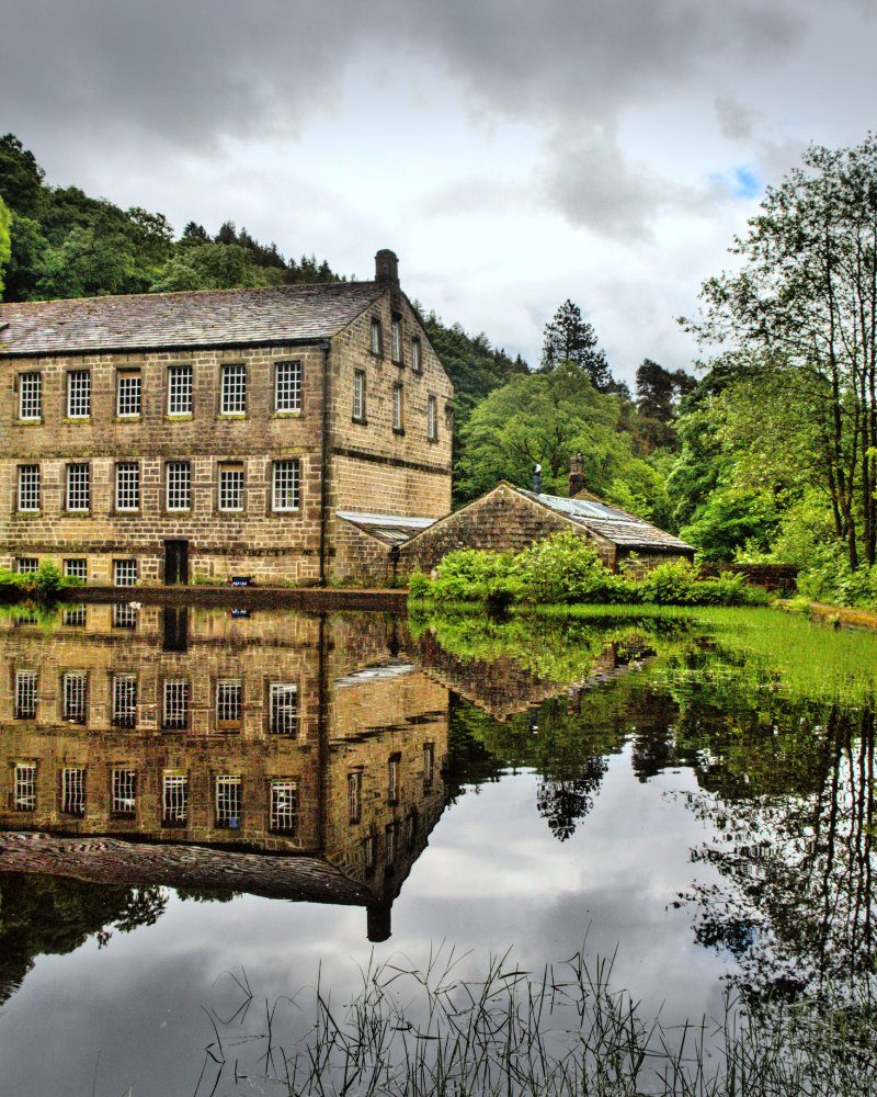 Landscape of Gibson Mill Museum by reflecting river in England with gray cloudy sky
